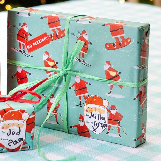Christmas-themed gift bags and boxes with Santa Claus design on a checkered tablecloth.