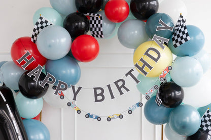 Balloon arch with 'Happy Birthday' text and racing theme decorations on a white wall.