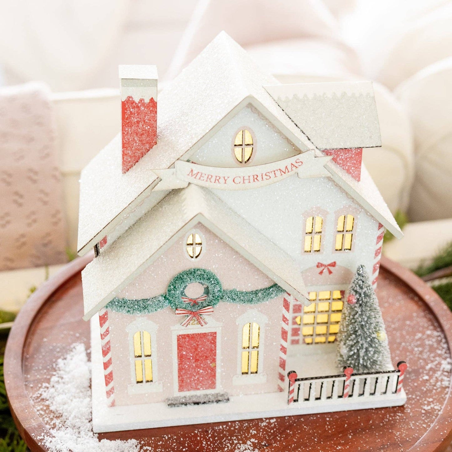 Decorative Christmas house ornament on a wooden base with a snowy effect.